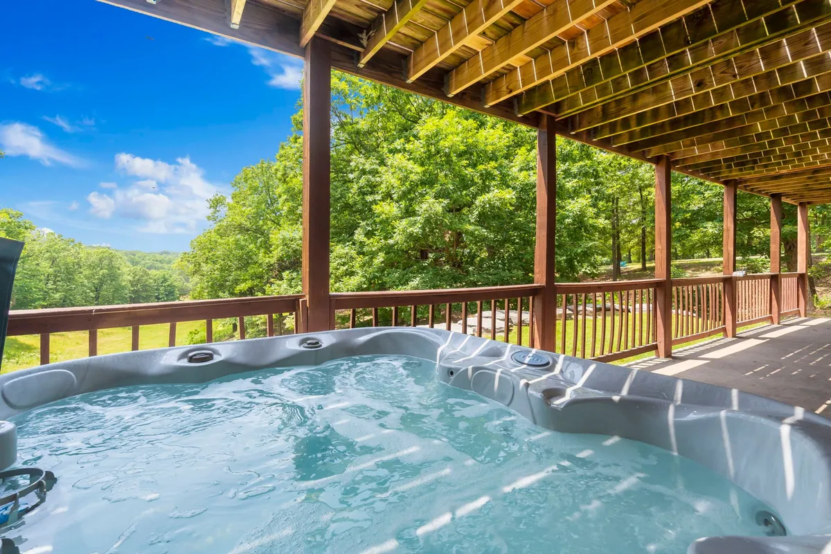 The lower-level outdoor deck features a bubbling hot tub surrounded by lush greenery, with space for guests to relax and take in panoramic Ozark views. The deck's private, tranquil vibe makes it the perfect extension of the fun happening inside.