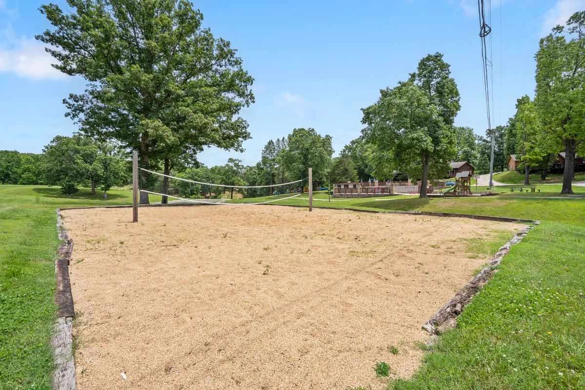 A sunlit sand volleyball court surrounded by trees and a few distant buildings, inviting guests to friendly matches and group activities outdoors.