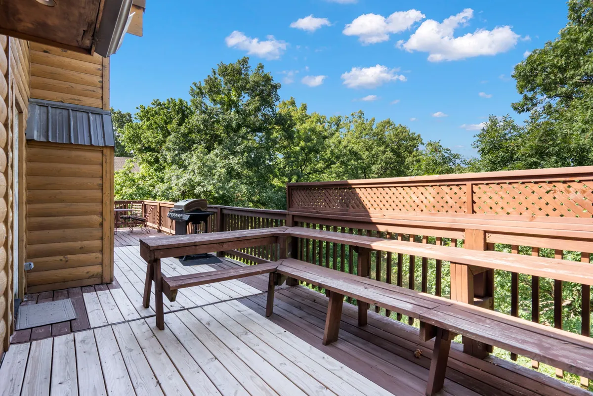 An exterior shot of the deck adjoining the main living space, featuring wooden benches, a grill, and lush greenery all around. The area is perfect for sunset views, outdoor meals, and unwinding with family or friends in a natural setting.