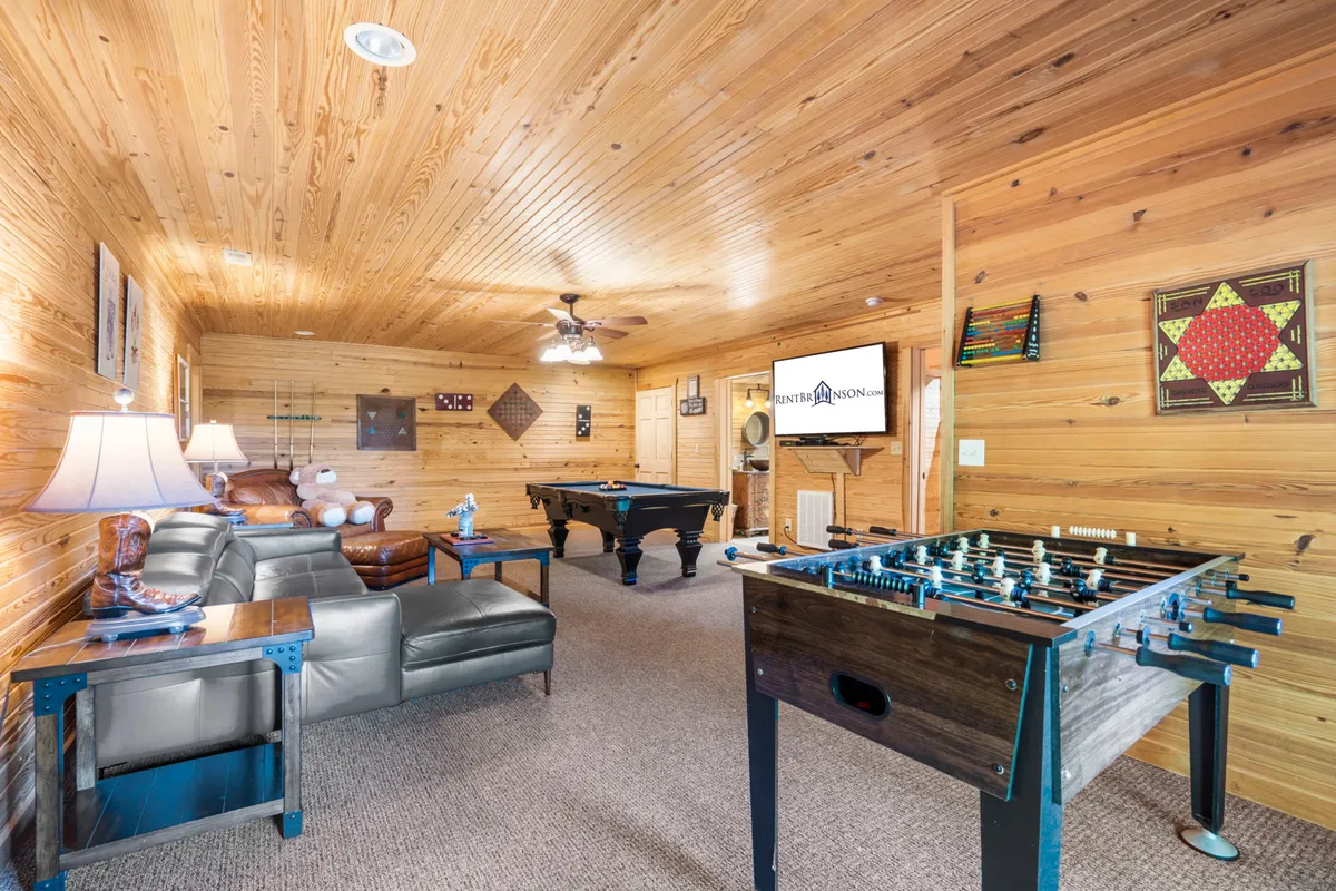 This interior scene showcases a lively game room featuring a pool table and foosball table, a comfortable sofa, a large television mounted on the wall, and playful decorative touches. The space is well-lit and arranged to foster fun, socializing, and friendly competition.