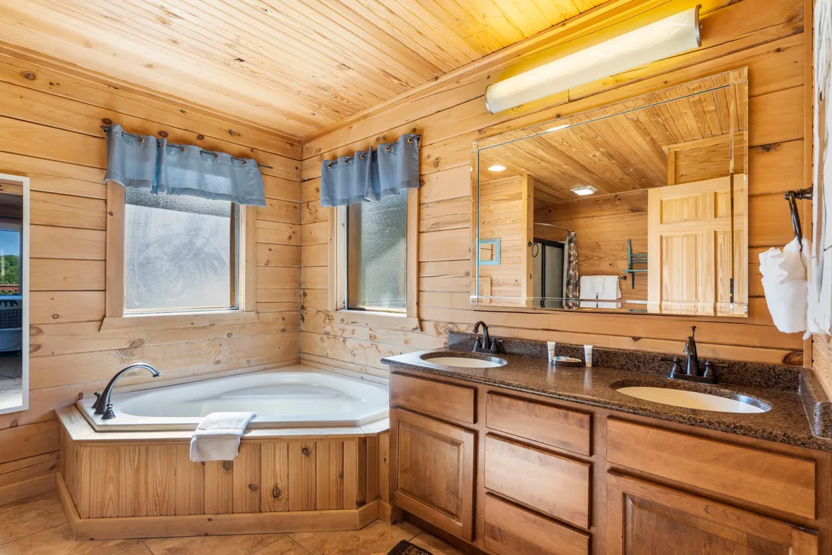 A tranquil bathroom featuring a jacuzzi tub, double sink vanity, wooden walls, and a large mirror. The space feels spa-like and soothing, ideal for self-care and relaxation.