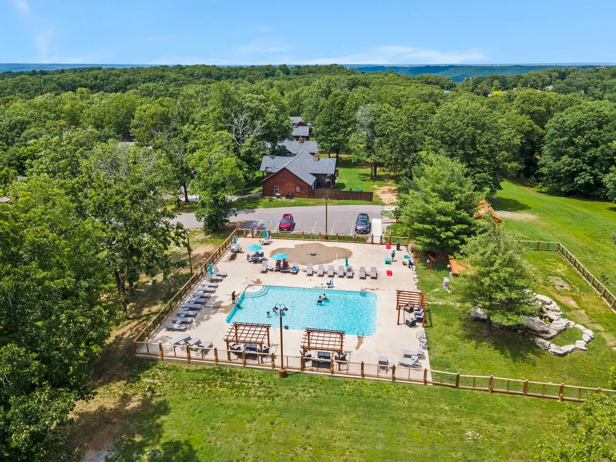 A vibrant swimming pool area with lounge chairs, cabana structures, and playful elements surrounded by trees. The pool offers a fun and luxurious retreat for guests to cool off, socialize, or simply relax in the sun.