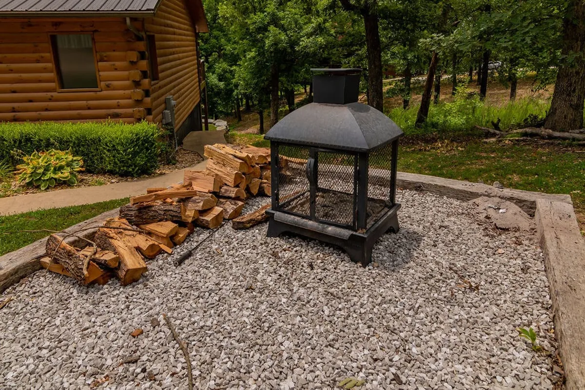 A welcoming fire pit area surrounded by natural gravel and stacked firewood, set against a backdrop of trees and greenery—perfect for storytelling and evening gatherings under the stars.