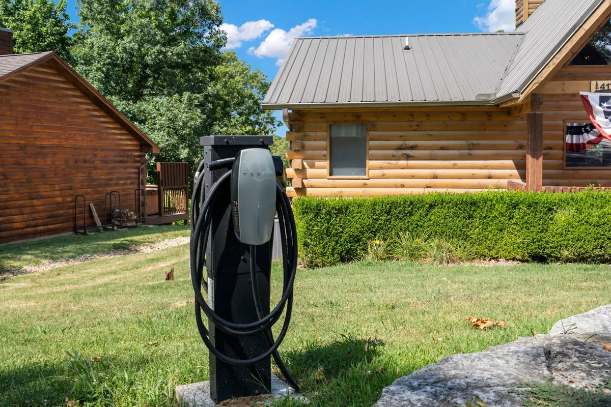 A modern electric vehicle charging station located beside a rustic log cabin, set on a well-maintained lawn. The image signals eco-friendly convenience for guests.