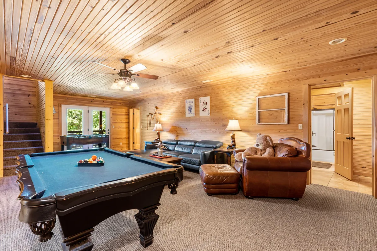 An inviting entertainment area with a pool table as the centerpiece, complemented by a leather sofa and a wooden ceiling that adds warmth. The arrangement evokes a cozy atmosphere ideal for relaxed evenings and friendly competition.